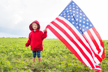 huge flag of United States of America in hands of a child in the background of a field of soybeans. USA celebrate 4th of July. Independence Day concept