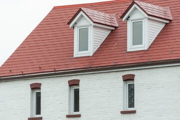 The corner of a red metal shingled roof with two raised dormers and three sunken small single...