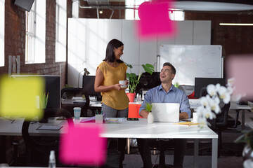 Happy caucasian male and female colleague talking in office, laughing and drinking coffee