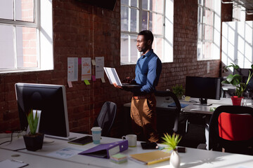 Serious african american businessman standing in sunny office using laptop