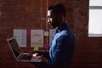 Serious african american businessman standing in office holding and using laptop