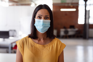 Portrait of caucasian businesswoman wearing face mask standing in office looking straight to camera
