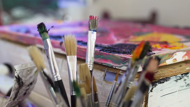 group of abstract used brushes next to an artistic painting. rack focus.