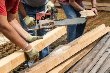Close up on hands of unknown men holding chainsaw at warehouse or construction site sawing and cutting lumber wood