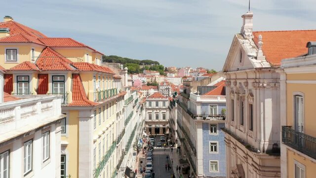 Drone camera flying forwards over street in level of surrounding buildings top floor. Aerial view of Rua Garrett, principal shopping street in Chiado. Lisbon, capital of Portugal.