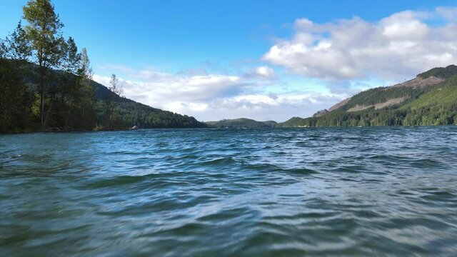 Clear water flying forward, revealing lake, distant rainforest green mountain hills with blue sky cloudsaerial drone shot in Lake Cushman Hoodsport Mason County Washington State Pacific Northwest