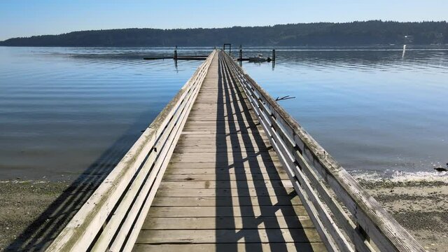 Flying through wood dock pier with danger sign over bright blue water and distant green trees over ocean coast aerial drone shot in Illahee Park Bremerton Kitsap Washington State Pacific Northwest