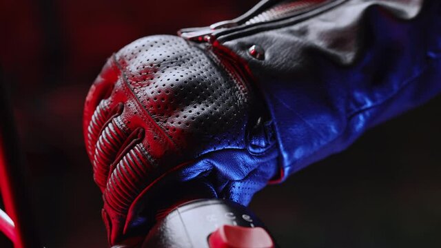  camera statically captures hand of driver in road gloves who twists accelerometer lever while standing at traffic light in night city. Nightlife and biker culture concept.