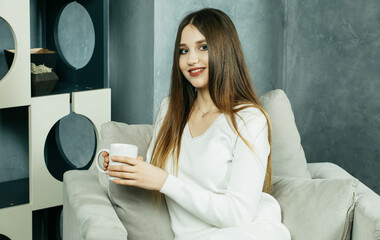 Beautiful young woman dressed in home suit holds a cup of tea or coffee in her hands