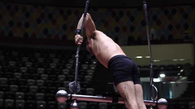 An acrobatic man leaning on one hand on the flying bar at circus