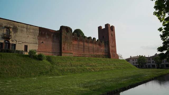 Lateral static view of walls of Castelfranco Veneto castle surrounded by lawn and moat. Italy