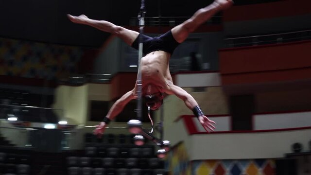 An acrobatic man showing a performance on the flying bar at circus - rotating without the support