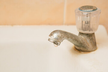 Water dripping from broken old and dirty faucet on the wash basin  and copy space