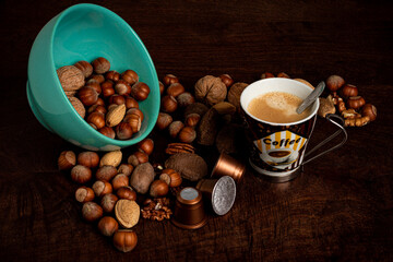 A cup of coffee, a green mug, nuts, almonds, hazelnuts and coffee capsules