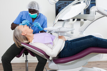 Mature female patient sitting in dental chair. Dentist is treating female patient. High quality...
