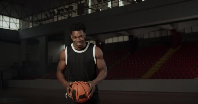 Video portrait of a basketball player bouncing a ball. African american man in uniform posing inside sports hall