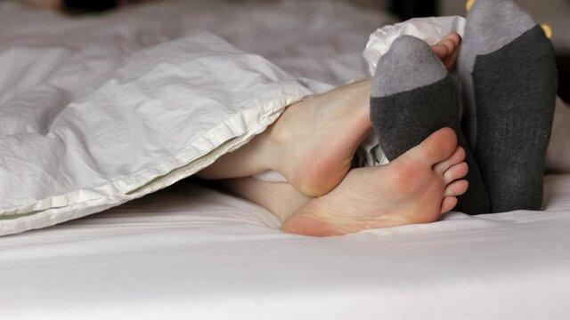 Happy couple in bed touching feet, socks and bare feet, rubbing together. 24FPS 4K.