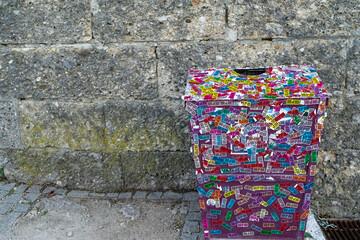 Colorful scarp of paper to stick around the bin or trash that obvious  is in front of the old block concrete wall at the public park for peple to leave the garbage in place.
