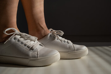 Close-up of female legs in white leather sneakers.