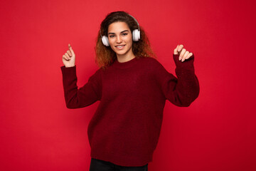 Beautiful happy smiling young brunette curly woman wearing dark red sweater isolated over red...