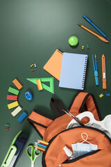 Office supplies in an orange school backpack lie on a green background. School supplies lie on the green chalkboard. Vertical, lot of free space for text. Education concept.