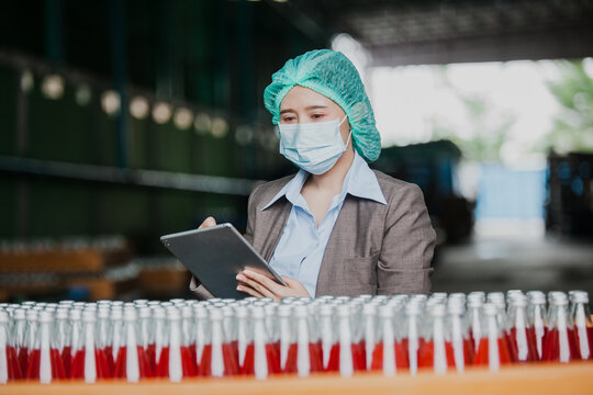 Female Inventory Manager with labtop is checking juice bottles before shipment. Inspection quality control. Manager inspecting production line at drinks production factory