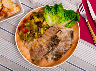 Juicy roast pork on a plate with a side dish of stewed vegetables, garnished with fresh lettuce leaves