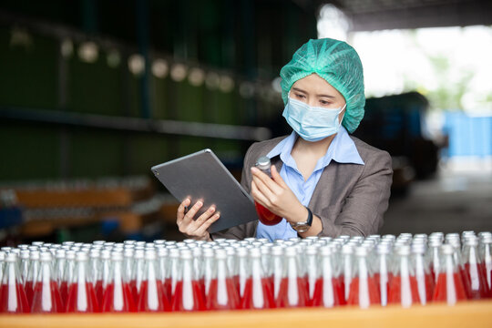 Female Inventory Manager with labtop is checking juice bottles before shipment. Inspection quality control. Manager inspecting production line at drinks production factory