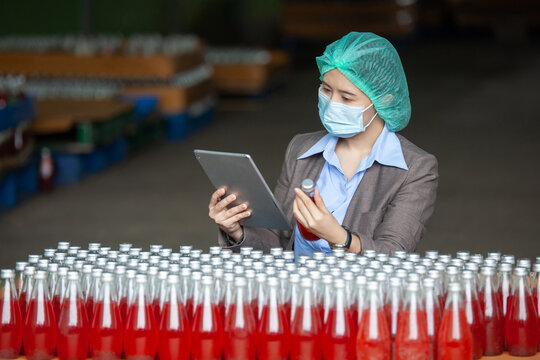Female Inventory Manager with labtop is checking juice bottles before shipment. Inspection quality control. Manager inspecting production line at drinks production factory