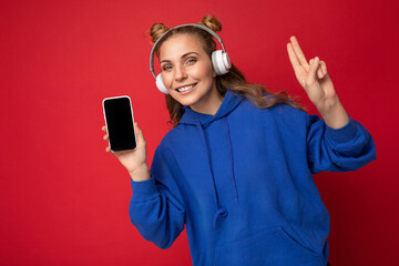 Photo of beautiful smiling young woman wearing stylish blue hoodie isolated over red background...