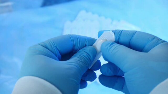 A professional doctor wearing blue medical gloves opens suppositories against the blue backdrop of many other drugs. A doctor shows how to open suppositories for the treatment of the disease. Close-up