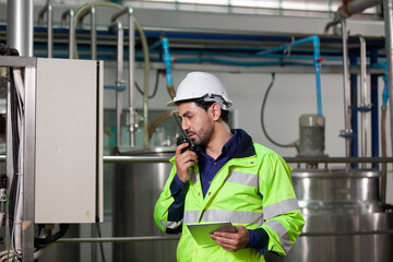 Engineer in uniform holding a tablet in her hands and conducting an inspection at the machine in Factory. Industrial production concept