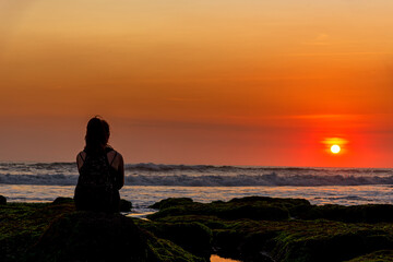 Silhouette of tourist sitting on a rock looking view the sunset over the sea in Bali, Indonesia.