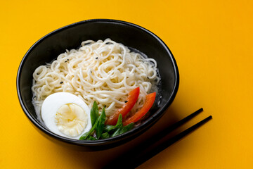 Black bowl of chineese fast cooked noodle with egg and vegetables. Black chopsticks near it at...
