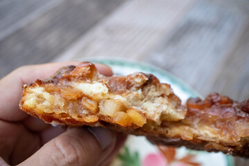 A hand holding n apple fritter pastry showing pieces of apples and cinnamon on the inside over a plate on a table