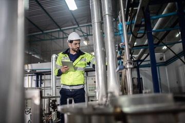 Engineer in uniform holding a tablet in her hands and conducting an inspection at the machine in Factory. Industrial production concept