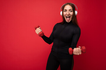 Attractive positive smiling young brunette woman wearing black sport clothes isolated on red...