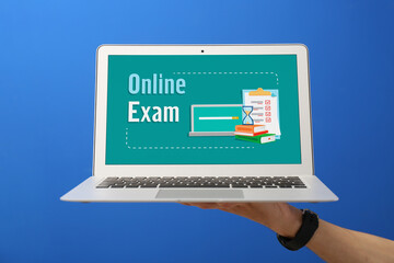Male hand holding laptop with text ONLINE TEST against color background