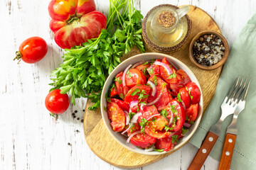 Summer snack or lunch. Fresh tomato salad with onions, herbs and olive oil on a white wooden table. Top view flat lay background.