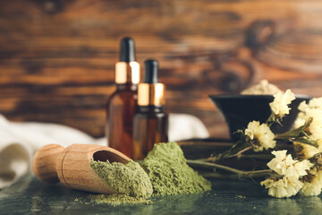 Dry henna powder in scoop and bottles of essential oil on wooden background, closeup