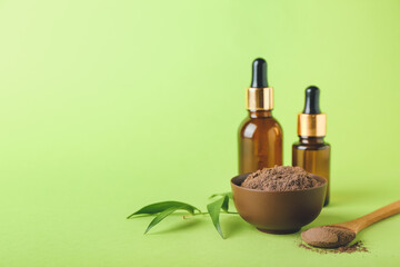 Dry henna powder in bowl and bottles of essential oil on color background