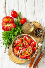 Summer snack or lunch. Fresh tomato salad with onions, herbs and olive oil on a white wooden table. Top view flat lay background. Copy space.