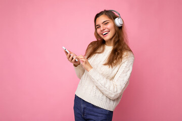 Photo shot of beautiful joyful smiling young female person wearing stylish casual outfit isolated over colorful background wall wearing white bluetooth wireless earphones and listening to music and