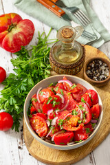 Summer snack or lunch. Fresh tomato salad with onions, herbs and olive oil on a white wooden table.