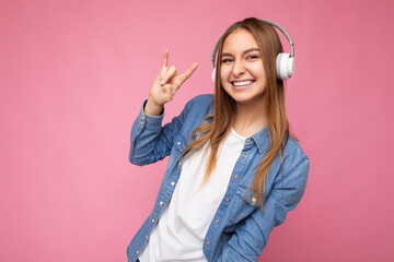 Photo shot of beautiful positive smiling young blonde woman wearing white wireless bluetooth...