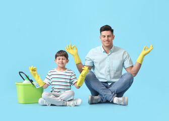 Father and son with cleaning supplies meditating on color background