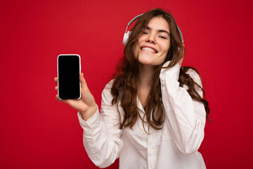 Attractive positive young brunette curly woman wearing white shirt isolated on red background wall...