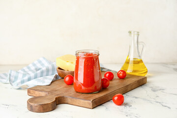 Obraz na płótnie Canvas Board with glass jar of tasty sauce, oil and cheese on light background