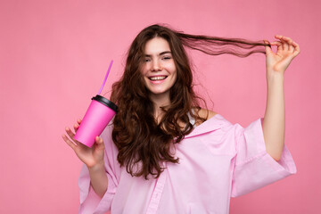 Naklejka premium Beautiful young positive brunette woman wearing casual stylish clothes isolated over colorful background wall holding paper cup for mockup drinking coffee looking at camera