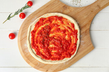 Pizza dough with tasty tomato sauce on light wooden background